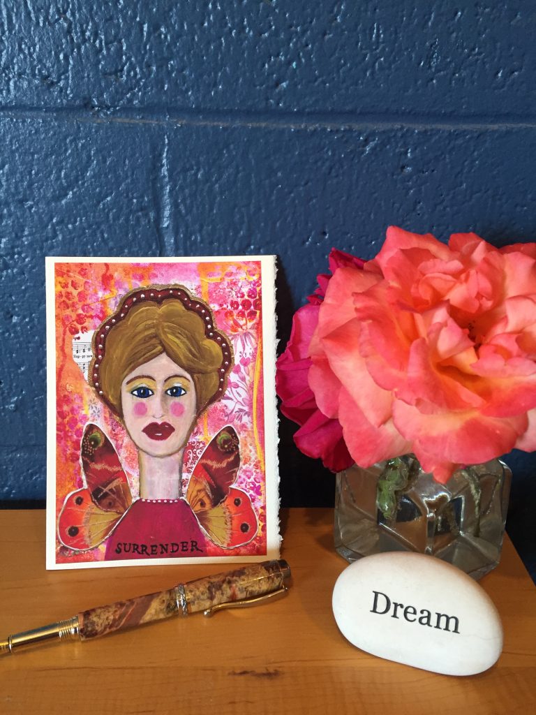 a surrender angel with a rose a rock that says "dream" and a fountain pen