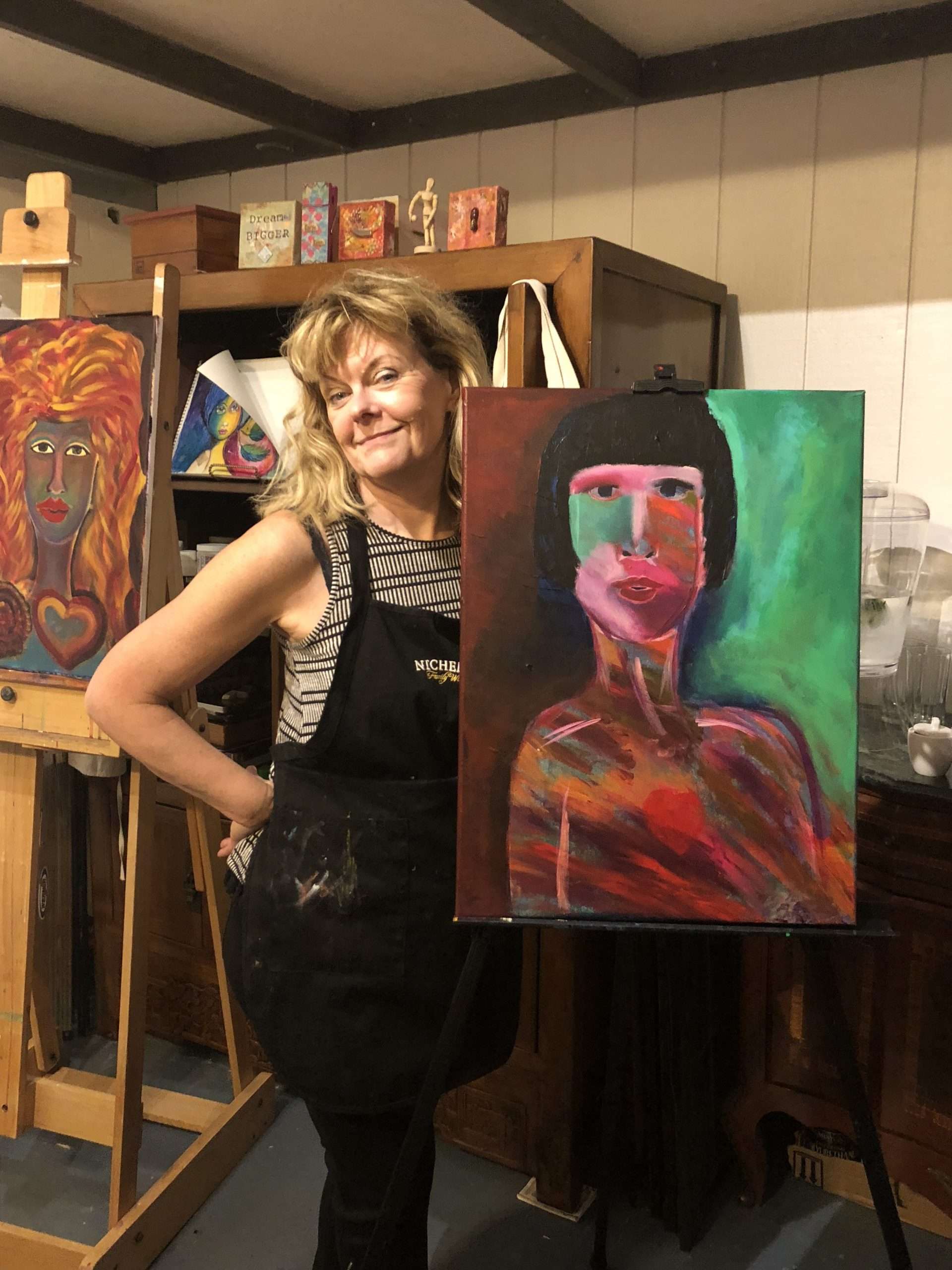 Kat Edman standing next to a painting of a work in progress on an easel