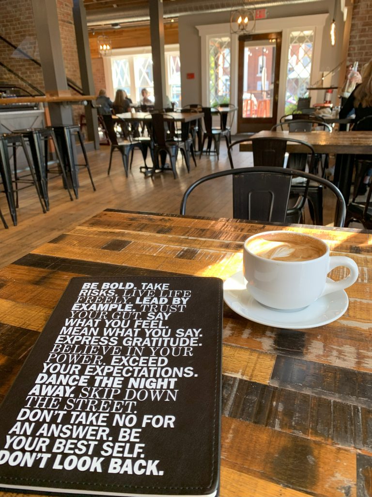 My journal with my coffee at a coffee shop. The journal cover is filled with inspiring quotes to create life with intention